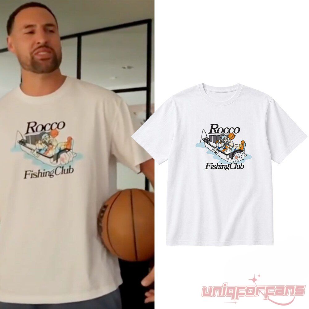 White graphic t-shirt featuring "Rocco Fishing Club" text and a cartoon illustration of a dog holding a basketball in a fishing boat